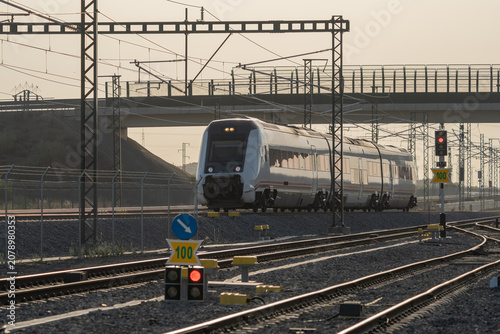 Commuter passenger train traveling on railway infrastructure during golden hour.
