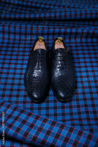 Male black leather shoes on dark blue checkered suit fabric background. Copy space for logo, design, advertising. Men's accessories