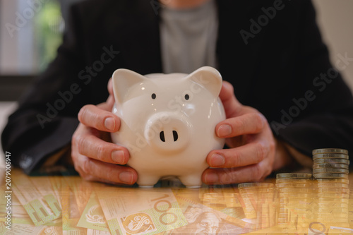 Businessman hands holding piggy bank and blurred Australian bank note and coins background in business finance and saving money investment concept, Save money and financial investment