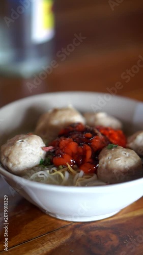 A bowl of traditional Indonesian beef meatballs with noodles, rice vermicelli, savory broth, chili sauce, and sweet soy sauce.