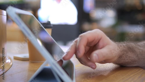 Close-up of a hand tapping a tablet screen. Hand rests on wooden surface. Background softly blurred, cozy warm lighting. Ideal for tech, digital work, or modern lifestyle content