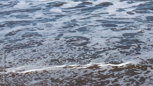 Canvas-taulu A close-up view of ocean water receding over dark wet sand, leaving behind delic