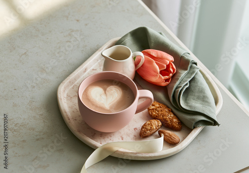 Pink cup with heart foam coffee tulip cookies and folded napkin on tray