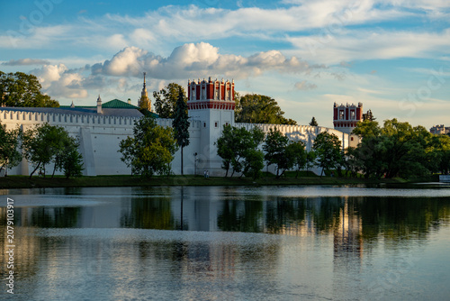 Epic Novodevichy convent ancient Russian orthodox architecture landscape panorama. 
Cinematic distant view of historic Moscow monastery fortress walls, 
golden domes, bell tower, green spring forest a