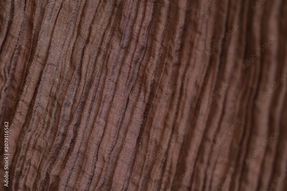 Obraz premium Macro shot of brown pleated and crinkled lyocell polyamide blend fabric texture. Detailed woven pattern and synthetic fiber structure with beautiful soft bokeh