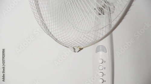 Female hand presses the power button to switch on an electric pedestal fan at home. Close-up of starting a household fan for cooling, ventilation and comfort during hot summer weather.
