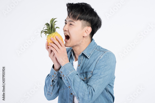 фотографія Playful young man pretending to bite a pineapple on light background