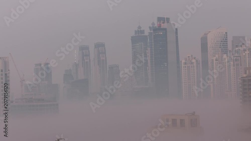 Fog blanketed city drone timelapse highlighting the architecture in Business Bay. A dense layer of morning fog blankets the lower structural foundations of the city. Massive scale.