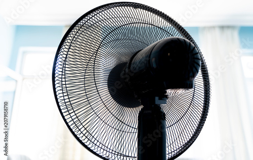 Electric pedestal fan inside a bright room against window light