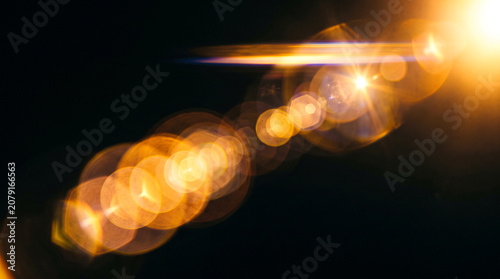 Golden bokeh light effect with glowing lens flare on dark background for abstract festive design