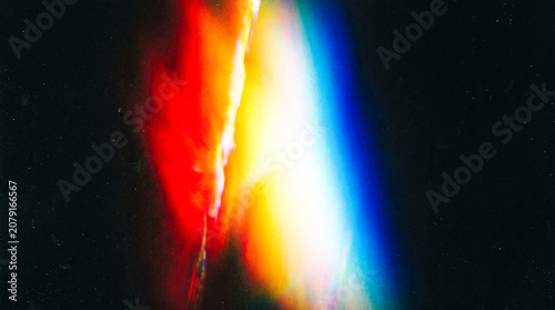 Abstract colorful light leak effect with vibrant red, yellow, and blue gradient on dark background