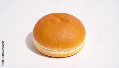 A single golden-brown hamburger bun with a smooth top and fluffy bottom placed on a plain light surface, highlighting its soft texture, simple form, and classic bakery appeal in minimal composition.