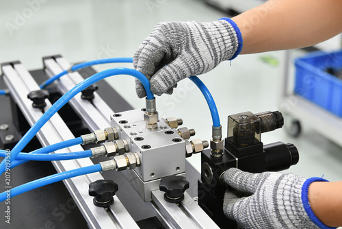 Technician's hands in gloves assembling pneumatic manifold system with blue tubes