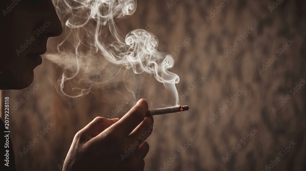 Fototapeta premium man holding smoking a cigarette in hand. Cigarette smoke spread. dark background