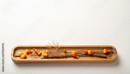 Minimalist Wooden Tray Arranged with Seasonal Candy Corn and Dried Botanical Elements on a Plain White Background