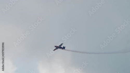 Stunt plane diving toward the left, aerobatic aircraft descending with a thin smoke trail against a grey sky, single engine sport plane at an air show, filmed in slow motion