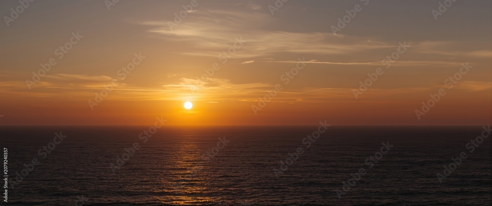 Fototapeta premium Sunset over the ocean with calm water and clouds