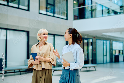 Foto Two diverse businesswomen walking and talking in a contemporary office building,
