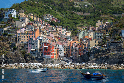Schilderij op canvas View from the sea of ​​Riomaggiore, one of the  Cinque Terre villages, a steep cascade of pastel houses descending towards a small harbor carved between dark cliffs