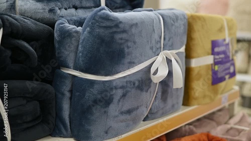 A person reaches for a blue blanket tied with a ribbon on a store shelf. The display shows various blankets stacked neatly, highlighting options for shoppers