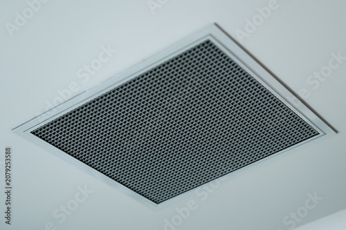 Low angle view of ceiling ventilation grille with geometric metal mesh on clean white indoor surface vent
