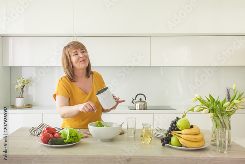 Attractive woman with olive oil in glass jar and organic vegetable on table in kitchen at home. Healthy food concept