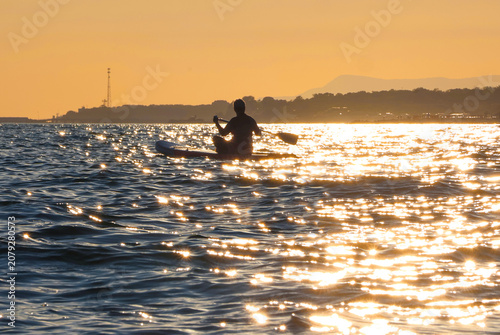 young women  riding  on sup surfing in the sea at sunset