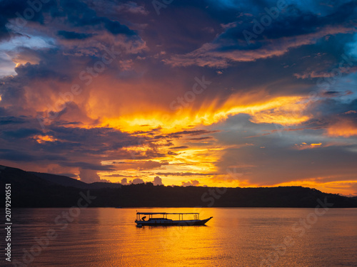 Vibrant sunset over Riung Bay and the 17 Islands Marine National Park, Flores, Indonesia, with traditional boats on calm water beneath dramatic orange, gold, and purple clouds