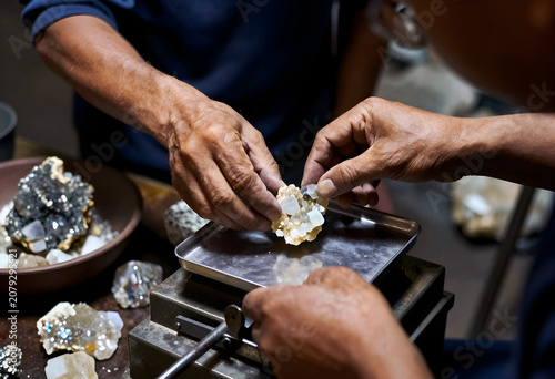 An artisan's hands carefully placing a raw, translucent selenite shard onto a velvet-lined wooden scale; the shard glows.