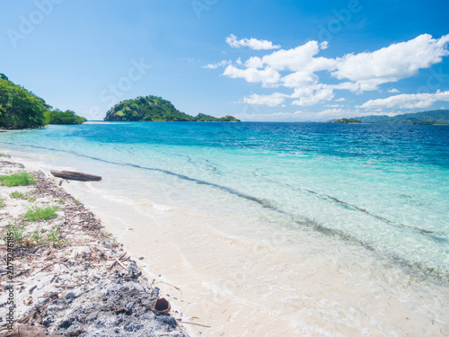 Pristine white sand beach and crystal-clear turquoise waters in Riung 17 Islands Marine Park, Flores, Indonesia, with small tropical islands on the horizon under a bright blue sky
