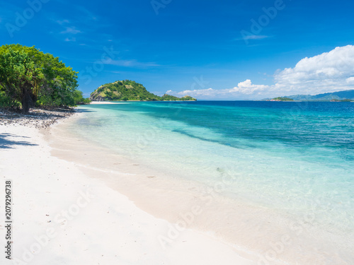 Pristine white sand beach and crystal-clear turquoise waters in Riung 17 Islands Marine Park, Flores, Indonesia, with small tropical islands on the horizon under a bright blue sky