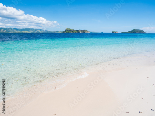 Pristine white sand beach and crystal-clear turquoise waters in Riung 17 Islands Marine Park, Flores, Indonesia, with small tropical islands on the horizon under a bright blue sky