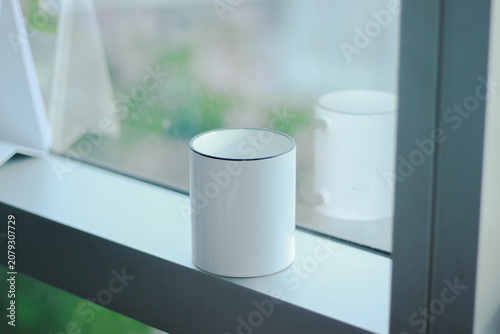 Minimal white ceramic mug mockup placed on a windowsill with soft natural light and a blurred background. Perfect for branding, logo presentations, product showcases, coffee shops, and e-commerce list