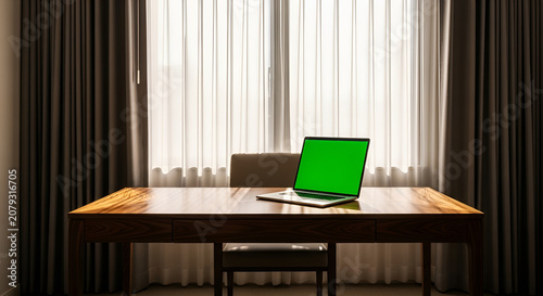 Empty workspace with laptop green screen on wood desk by bright window and sheer curtains