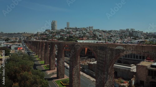 Iconic arches of Queretaro frame ascending aerial view unveiling apartment buildings and contemporary urban development behind monument