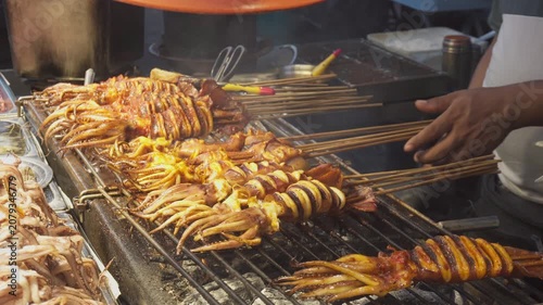 Street vendor is grilling squid satay at a food market