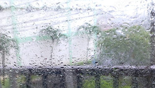 View of raindrops and water streaks covering a glass window during a rainy day. The scene outside appears softly blurred, this image conveys themes of rainy weather, seasonal rainfall, moisture, calm 