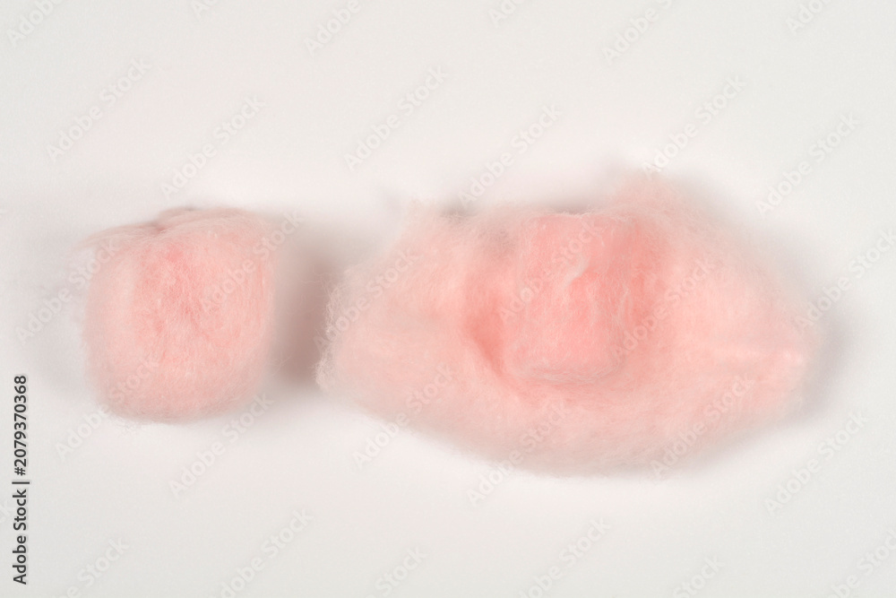 Fototapeta premium Top view of two soft pink wax earplugs wrapped in protective fluffy cotton wool fibers on a seamless white surface.