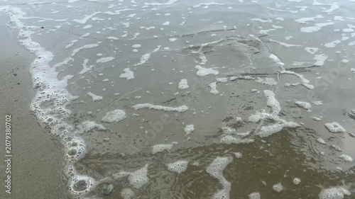 Close up of gentle ocean wave and white sea foam on a sandy beach