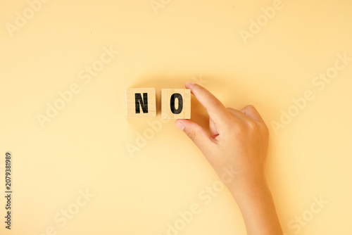 Hand arranging wooden letter blocks spelling NO on a bright background. Concept of rejection, refusal, decision making, boundaries, risk management and personal choice.