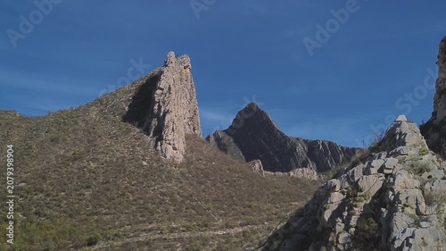 Majestic rocky mountain peaks filmed from aerial perspective with clear blue sky backdrop, camera slowly rotating around dramatic geological formations highlighting natural grandeur