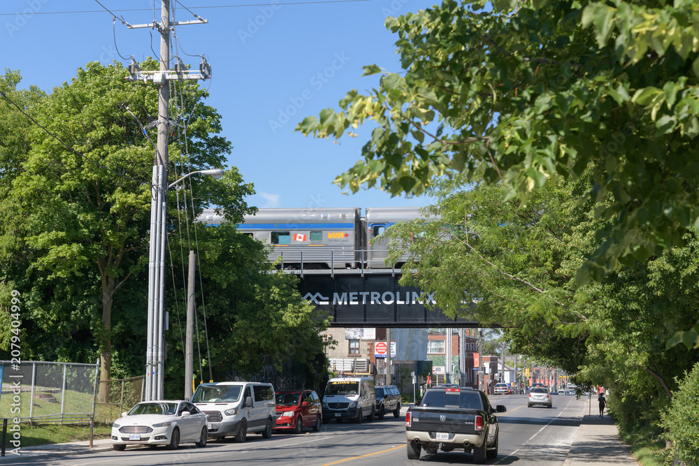 Obraz premium looking west on Rogers Rd to Go Barrie line with VIA Rail passenger cars runny by, Toronto