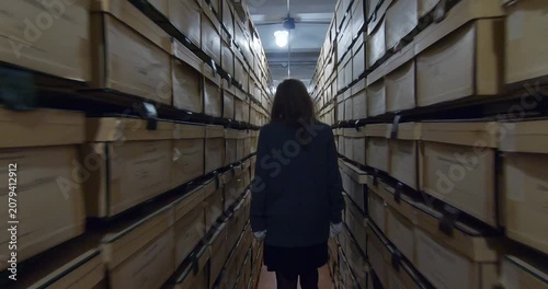 Document storage area. An archivist walks between rows of shelving units filled with folders and boxes.