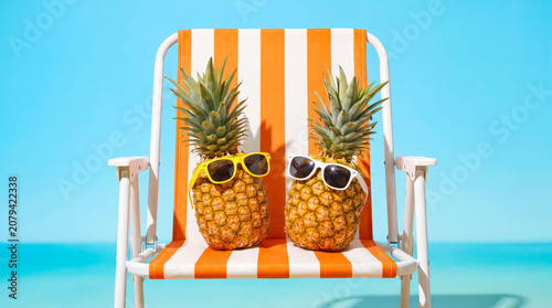 Two pineapples with sunglasses sitting on a striped beach chair