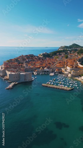 Epic Dubrovnik old town ancient castle architecture vertical aerial panorama. 
Cinematic drone panning flight of medieval stone fortress walls, 
terracotta roof tiles and blue Adriatic sea coast in Cr