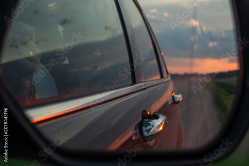 Freedom and travel concept with scenic orange sunset clouds reflected in automobile wing mirror on a rural evening way