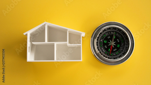 Quadro su tela Top down view of an open white miniature house architectural floor plan next to a classic magnetic compass isolated on a yellow background