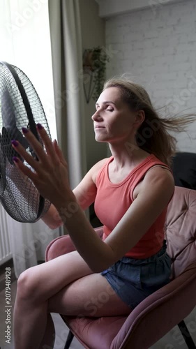 Woman enjoying wind from electric fan. Hair is blowing. Air conditioning and cooling at home on summer heat