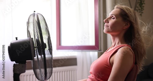 Woman enjoying wind from electric fan. Hair is blowing. Air conditioning and cooling at home on summer heat. Hot weather