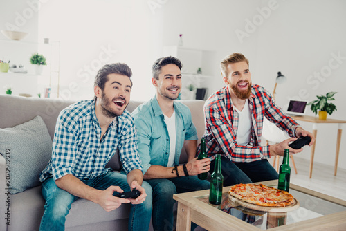 Bild auf Leinwand Three friends playing video games and enjoying pizza and beer in a cozy living r